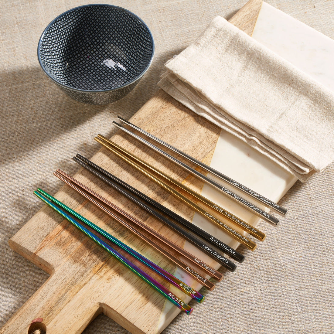 Personalised metal chopsticks in rainbow, gold, rose gold, black and silver on a wooden board