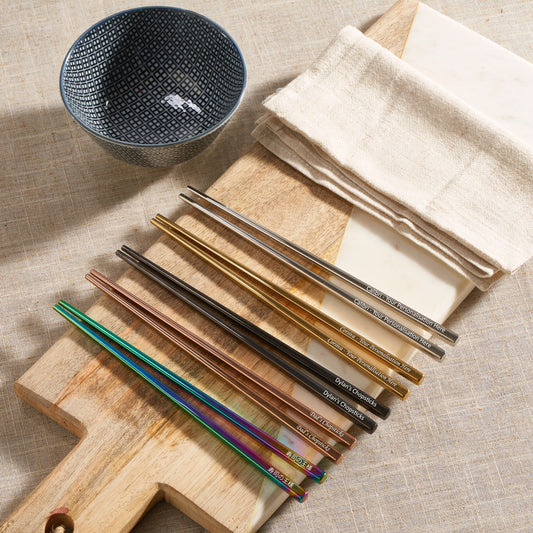 Personalised metal chopsticks in rainbow, gold, rose gold, black and silver on a wooden board
